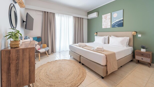 A hotel room with a bed, a desk, a chair, a round rug, and artwork on the walls. - Residence City Frida (Rodos)