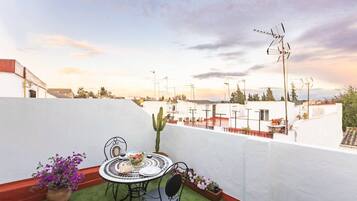 Une terrasse sur le toit, avec une table ronde et des chaises, entourée de plantes en pot et d’un cactus.
