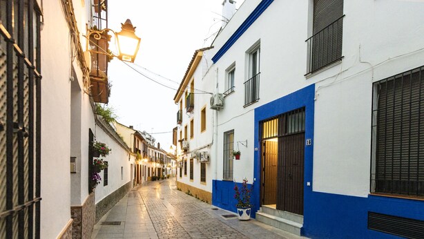 A narrow cobblestone street lined with buildings featuring traditional architecture, a street lamp, and hanging flower baskets. - 3 BD house with Private Solarium and patio (Cordoba)