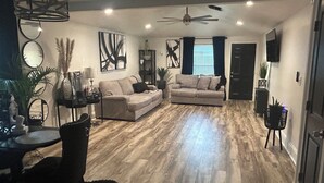 A modern living room with a sofa, a dining table, and a ceiling fan. - Charming 3-bedroom house in LaPlace with AC, WiFi (LaPlace)