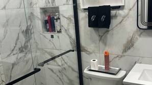A bathroom with a glass-enclosed shower, a toilet, a sink, and a mirror. - Charming 3-bedroom house in LaPlace with AC, WiFi (LaPlace)