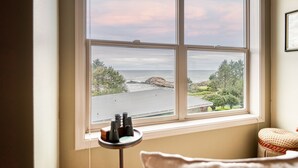 Ein Zimmer mit großem Fenster mit Blick auf eine Küstenlandschaft, einem kleinen Tisch mit Fernglas und einem gepolsterten Stuhl.