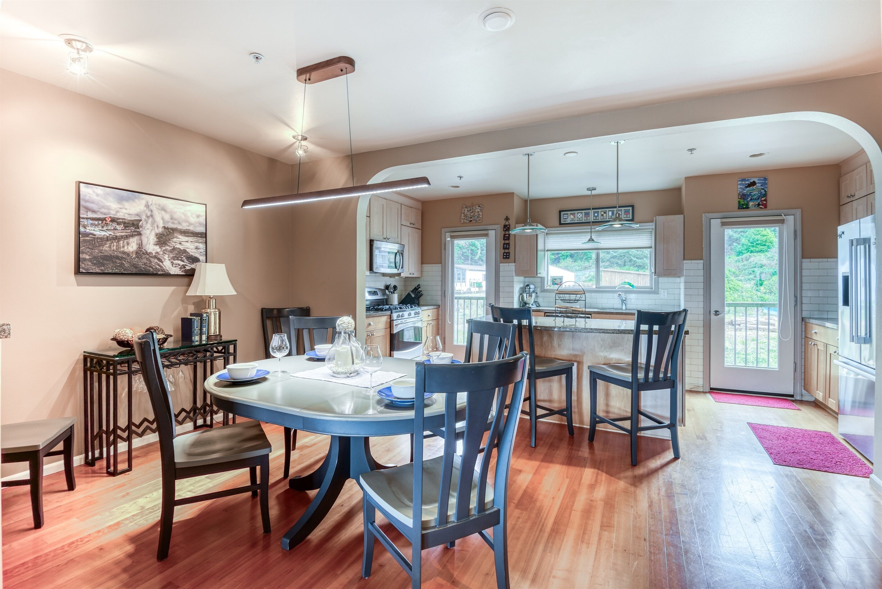 A modern kitchen with a dining area, featuring a central island, wooden cabinets, and a view of the outdoors.