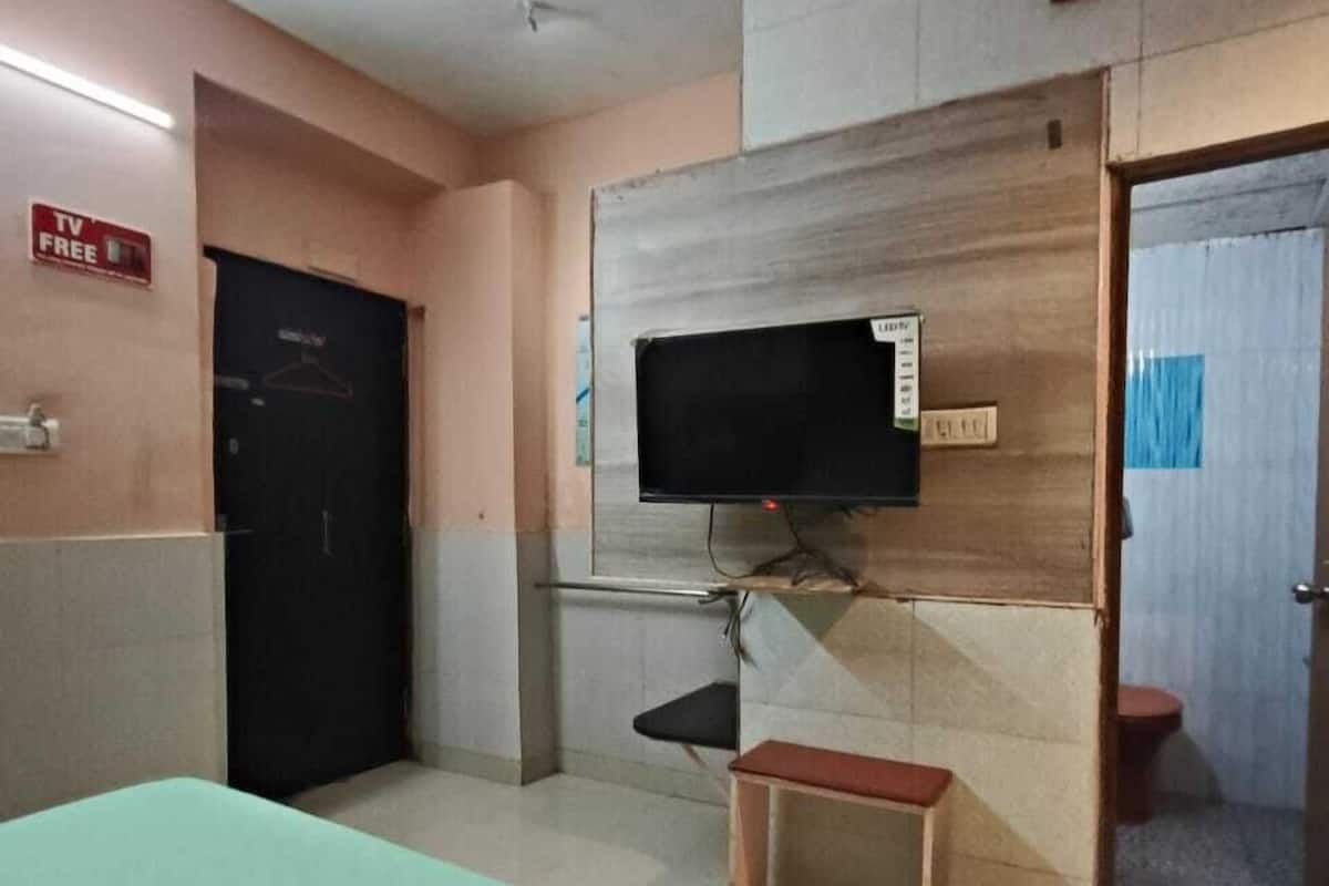 Una camera d'albergo con un letto, una TV fissata al muro, uno sgabello di legno e una porta che dà su un bagno.