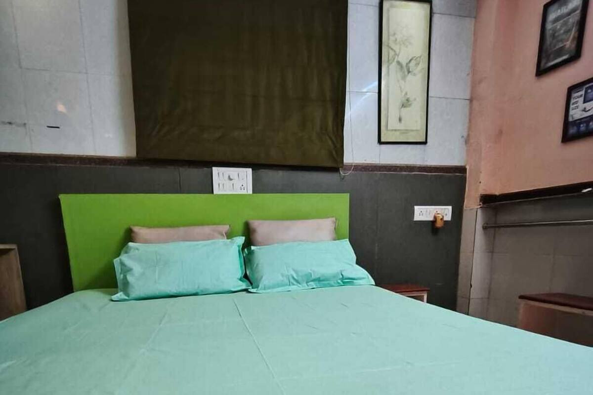 Un letto con testiera verde e biancheria azzurra, una lampada a parete e un quadro incorniciato sopra il letto.
