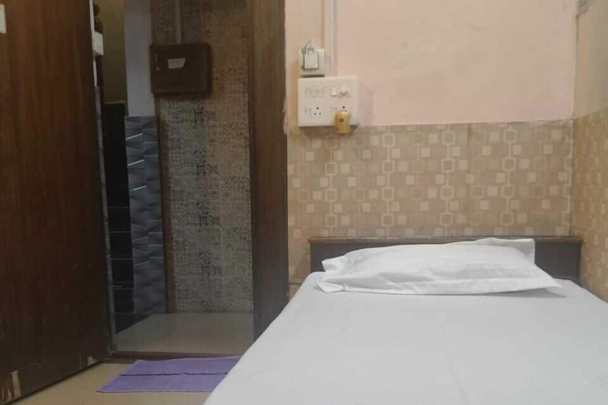Una camera d'albergo con un letto, una porta, una presa elettrica e una parete piastrellata.