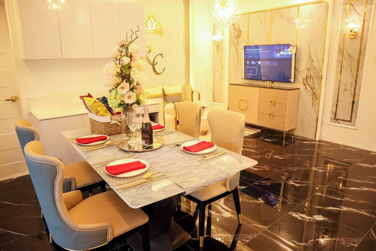 Un coin repas avec une table en marbre, des chaises de couleur beige et un téléviseur fixé au mur.