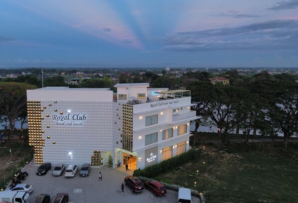 A hotel named "Royal Club" with a modern design, featuring multiple floors and a parking area with several cars.
