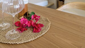 Une table avec une bouteille de vin, deux verres à vin et des fleurs roses sur un set de table en fibres tressées.