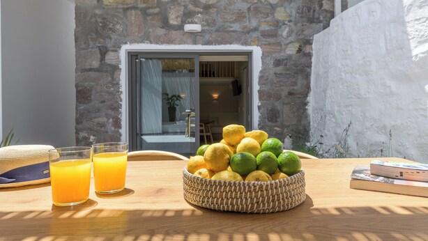 Un panier en osier rempli de citrons et de citrons verts est posé sur une table en bois, accompagné de deux verres de jus d’orange.