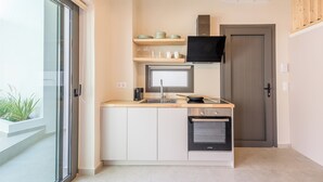 Une cuisine compacte équipée d’un four encastré, d’un four à micro-ondes et d’un évier. Une étagère en bois se trouve au-dessus de l’évier et un téléviseur est fixé au mur.