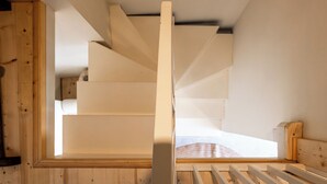 Un escalier avec une rampe en bois, et en arrière-plan, on aperçoit un lit.