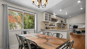 A dining area with a wooden table and chairs, a chandelier, and a kitchen in the background. - Desert Dreams Retreat Hot Tub Game Room Fire Pit (Sparks)