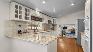 A modern kitchen with white cabinetry, a granite countertop, and a built-in oven. - Desert Dreams Retreat Hot Tub Game Room Fire Pit (Sparks)