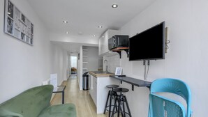 A modern kitchen with a flat-screen TV, a bar area with stools, and a green sofa. - Ecclesall Road Apartment (Sheffield)