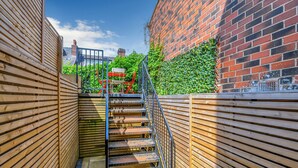 A wooden staircase leading to a rooftop area with a red chair and table, surrounded by brick walls and greenery. - Ecclesall Road Apartment (Sheffield)