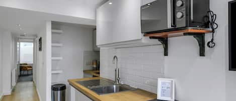 A modern kitchen with a wooden countertop, stainless steel sink, and a microwave mounted on a wooden shelf.