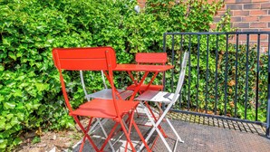 A set of red and white folding chairs and tables arranged outdoors, with a brick wall and green foliage in the background. - Ecclesall Road Apartment (Sheffield)