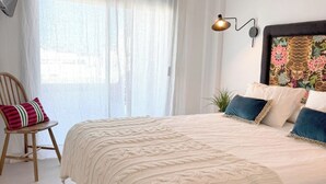 Een slaapkamer met een groot bed, een aan de muur bevestigde televisie en een raam met dunne gordijnen.