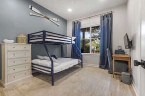 A bunk bed room with a dresser, a window with curtains, and a wall-mounted TV. - Le Rêve Charmant | A Serene Gulf Coast Hideaway with Golf Cart Provided (Gulf Shores)