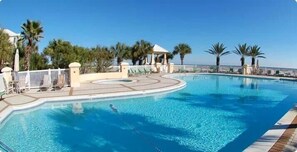 A swimming pool with a curved edge, surrounded by palm trees and lounge chairs. - Le Rêve Charmant | A Serene Gulf Coast Hideaway with Golf Cart Provided (Gulf Shores)