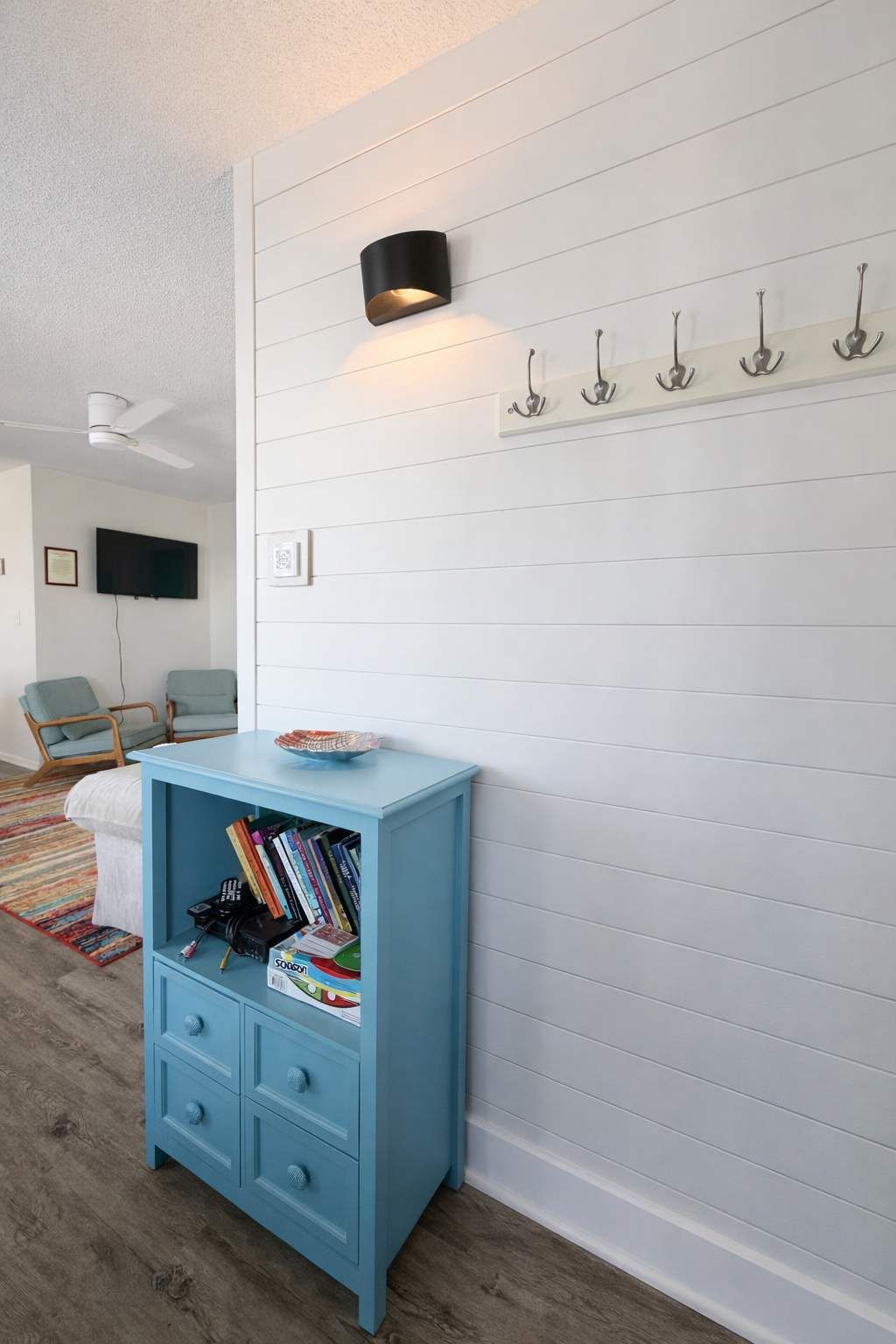 Una habitación con un armario azul claro, un ventilador de techo, un televisor montado y una lámpara de pared.