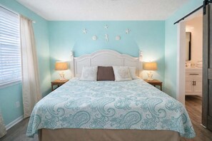 A bedroom with a bed, two bedside tables, a nightstand, a window with curtains, a wall with star decorations, and a door leading to another room.