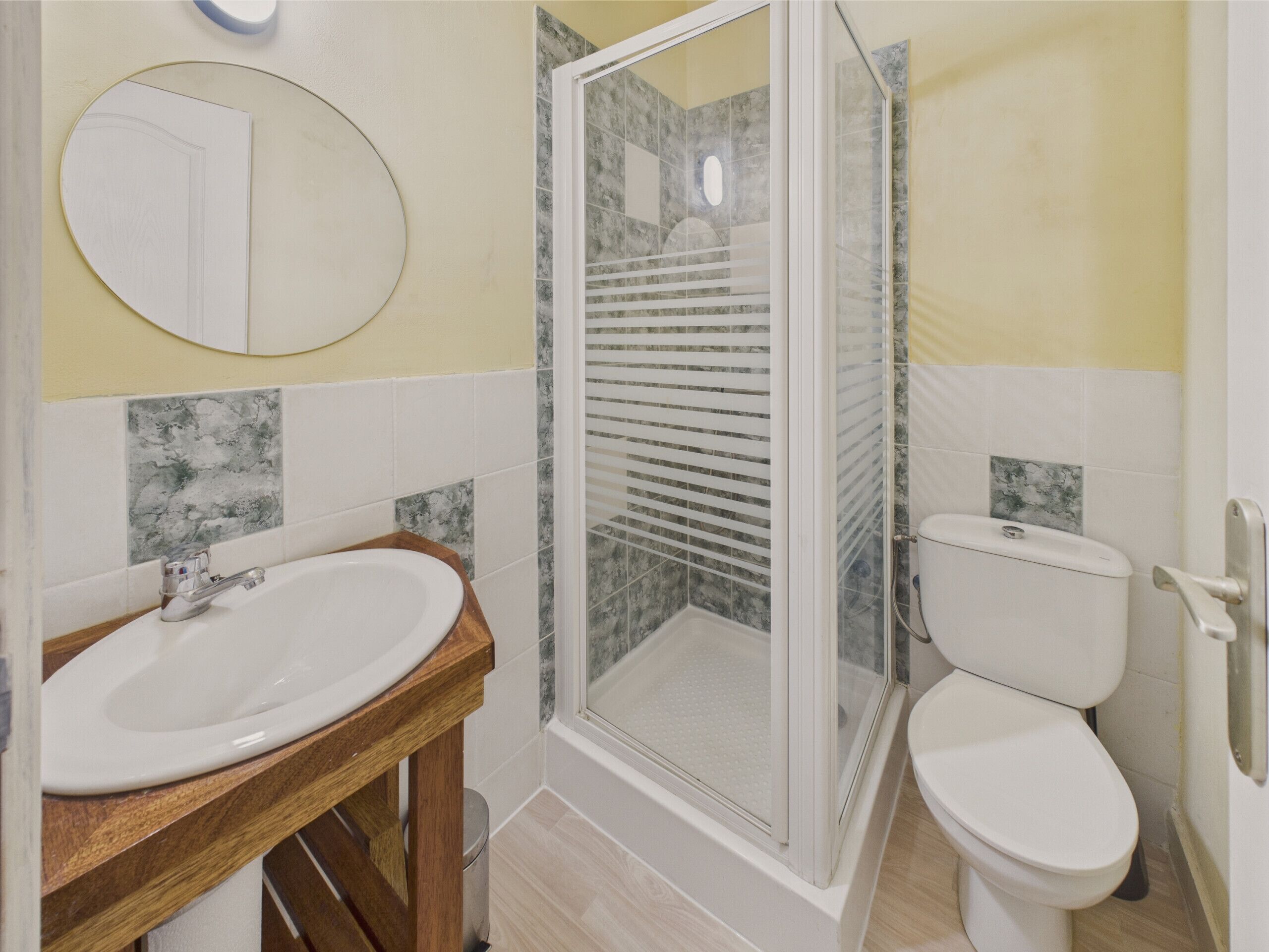 A bathroom with a wooden vanity, a white sink, a toilet, and a glass-enclosed shower.