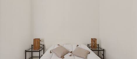 Une chambre au décor minimaliste, avec un lit, deux tables de chevet et un panier tressé sur chaque table de chevet.