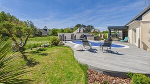 En baghave med swimmingpool, liggestole og en overdækket patio.