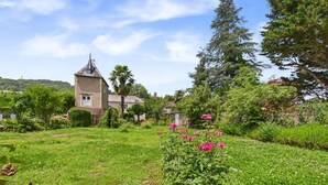A historic building with a tower, surrounded by lush greenery and flowering plants.