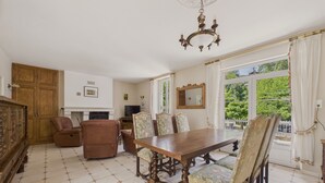 A dining area with a wooden table and chairs, a fireplace, and a view of greenery outside.