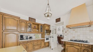 A kitchen with wooden cabinets, a white countertop, a stove, and a dining area with a table and chairs.
