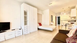 A modern living room with a flat-screen TV, a sofa, a bed, and a kitchenette. - Studio in front of the pool (Marbella)