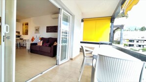 A balcony with a yellow blind, a white table, and a brown sofa in the background. - Studio in front of the pool (Marbella)