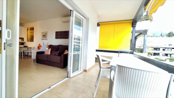 A balcony with a yellow blind, a white table, and a brown sofa in the background. - Studio in front of the pool (Marbella)