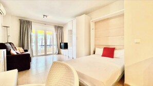 A hotel room with a bed, a sofa, a TV, and a balcony with curtains. - Studio in front of the pool (Marbella)