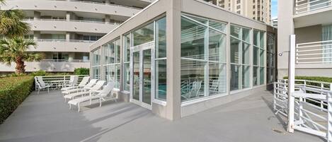 A modern building with a glass facade, outdoor seating area, and a palm tree.