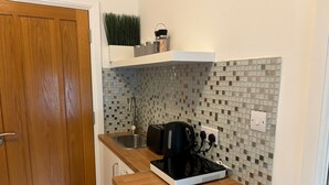 A compact kitchen with a wooden door, a sink, a countertop, a black coffee maker, and a tiled backsplash. - compact studio in central location with excellent transport links. (London)