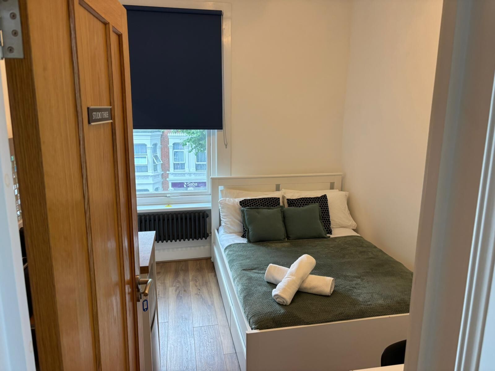 A small, neatly arranged bedroom with a bed, pillows, and a rolled towel.