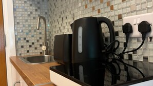 A kitchen with a modern design, featuring a tiled backsplash, a stainless steel sink, and a black electric kettle on a white countertop. - compact studio in central location with excellent transport links. (London)