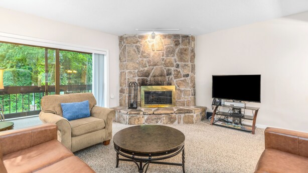 A living room with a stone fireplace, a flat-screen TV, and leather sofas. - Holly Ridge 204 | Near Gatlinburg + Cozy (Gatlinburg)