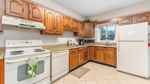 A kitchen with wooden cabinets, a white stove, a microwave, and a refrigerator. - Holly Ridge 204 | Near Gatlinburg + Cozy (Gatlinburg)
