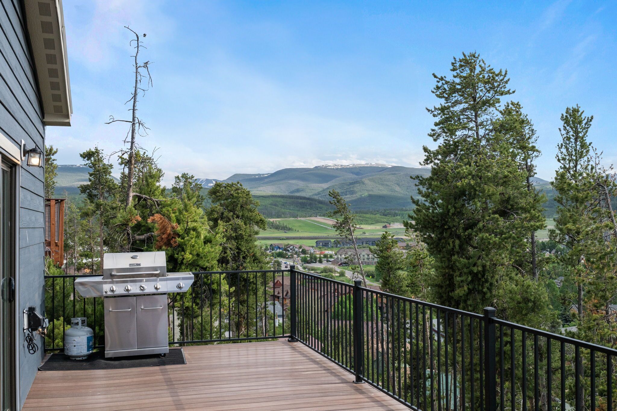 A balcony with a grill, a gas tank, and a view of a mountainous landscape.