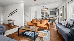 Ein geräumiges Wohnzimmer mit einer Couch, einem Couchtisch und einem Deckenventilator. Eine Treppe führt zu einer weiteren Ebene.