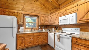 Une cuisine avec des meubles en bois, un réfrigérateur blanc, un four à micro-ondes, une cuisinière et une fenêtre donnant sur un paysage verdoyant.