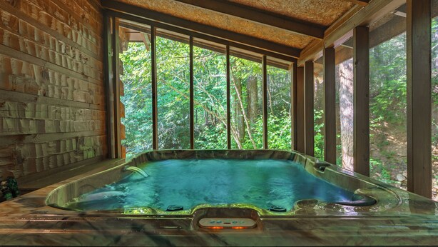 Un bain à remous avec un intérieur en bois et de grandes fenêtres donnant sur une forêt.