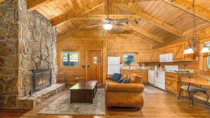 L’intérieur chaleureux d’un chalet avec une cheminée en pierre, un plancher en bois, un canapé en cuir et un coin cuisine.