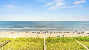 Ein Strand mit einer Holzpromenade, die zum Ufer führt, feinem Sand und dem Meer.