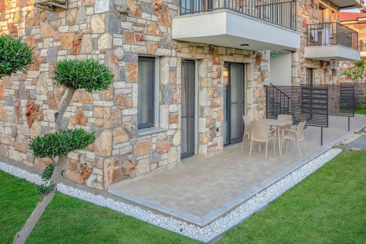A stone building with a balcony, a patio area with chairs, and a small garden.